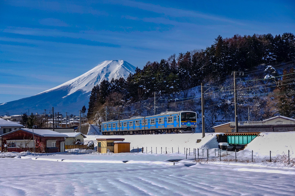 冠雪した富士山と一面の銀世界を走る富士急行線
